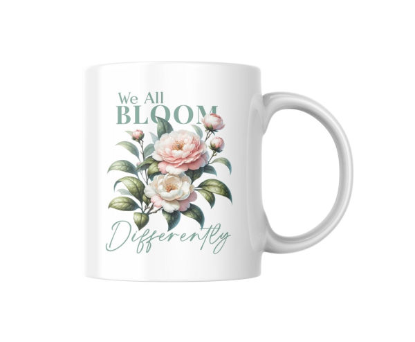 Weiße Keramiktasse mit botanischem Design und dem Zitat „We All Bloom Differently“, freigestellt auf weißem Hintergrund.